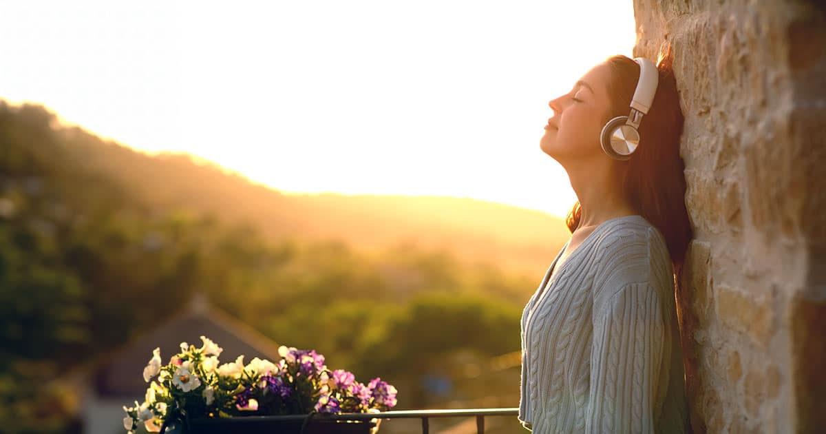 Woman leaning on balcony wall listening through headphones