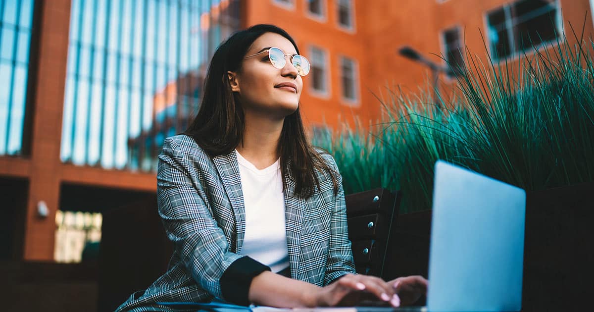 Woman looking up and around outdoors while using laptop