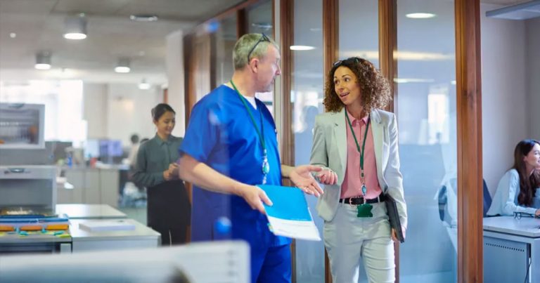 Woman walking through office talking to man in scrubs