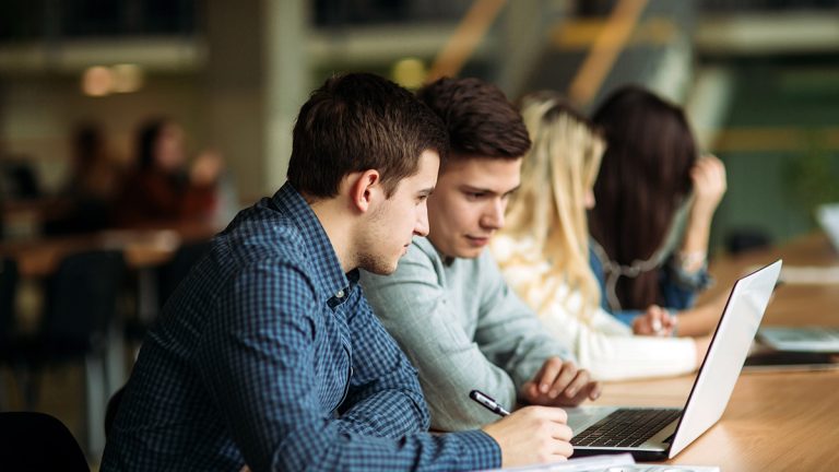 Business students working together at a laptop in a classroom or study area.