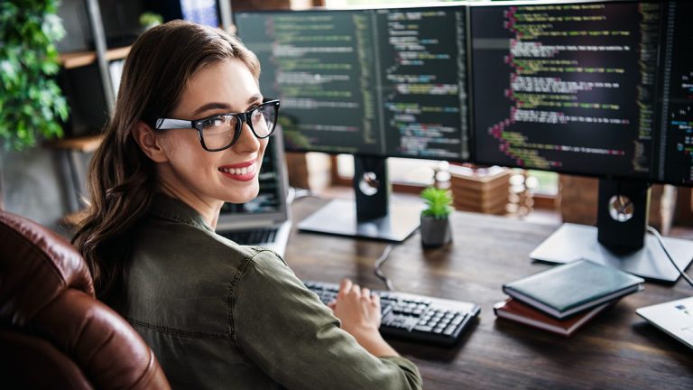 Woman at a computer workstation with programming code displayed across multiple monitors.