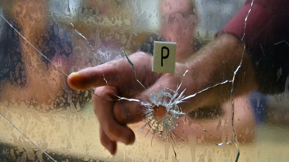 Hand reaching through shattered glass beside a crime scene evidence marker