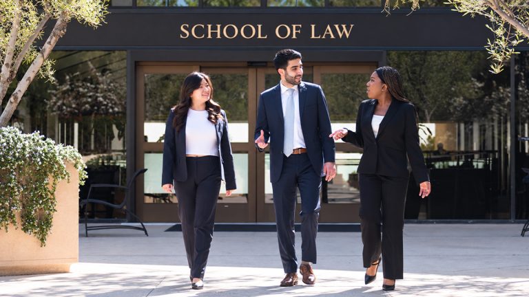 Three law degree students in business attire walking and talking outside a law school.