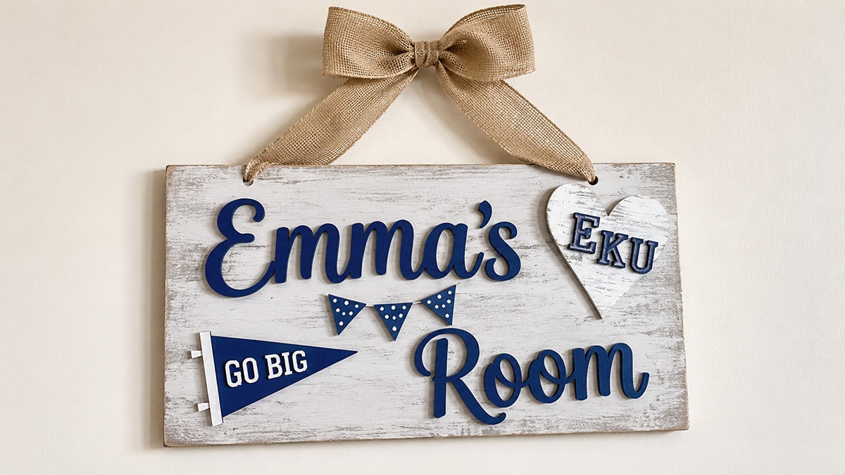 Personalized wooden dorm room sign reading “Emma’s Room” with blue lettering, college pennants and a burlap bow