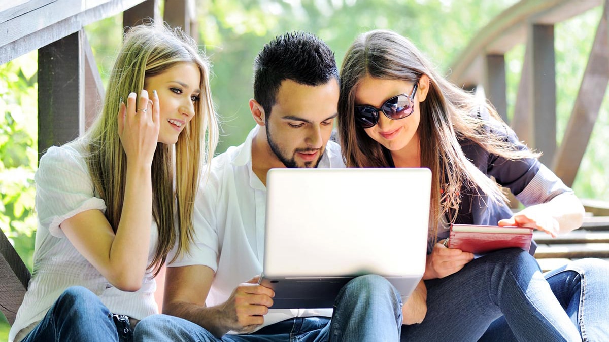 University students using a laptop together outdoors while studying and collaborating for success in online classes.