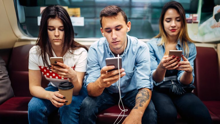 Three university students using smartphones while seated together on public transport.