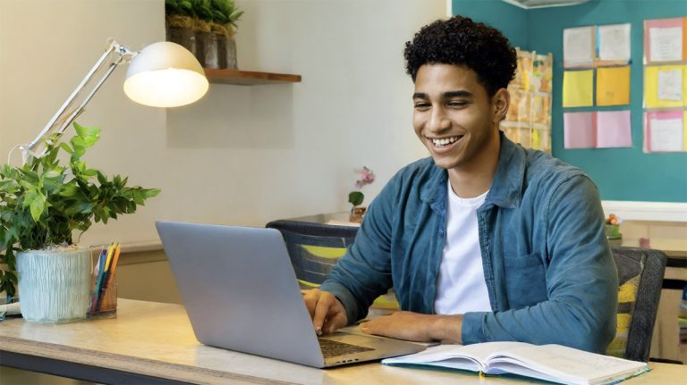 College student taking an online class on a laptop in his dorm room