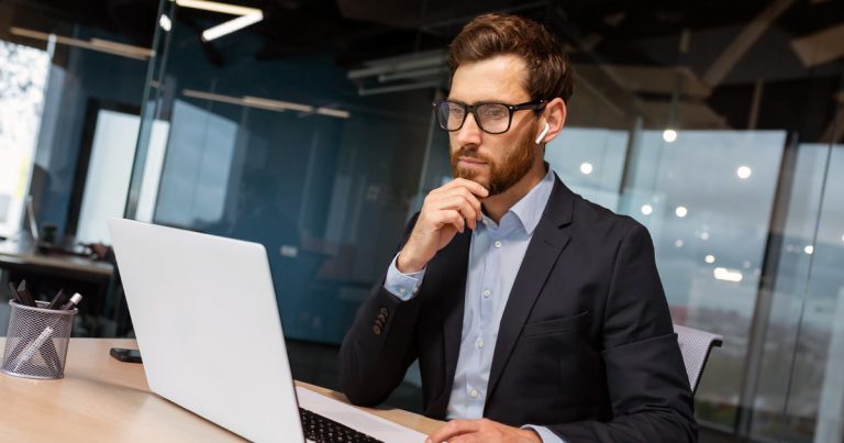 Businessman working in office with earbuds and a laptop