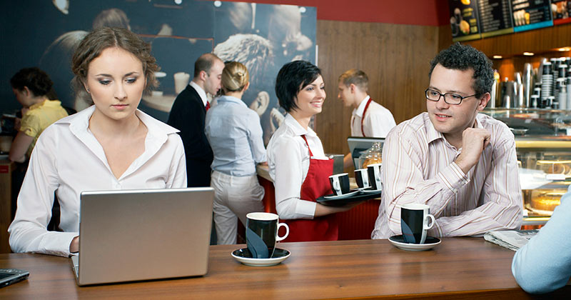 Woman typing on a laptop in a busy cafe